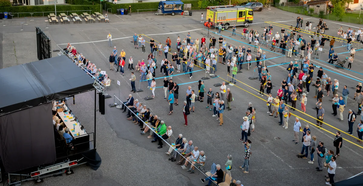 Menschen stehen versammelt vor einer Bühne.